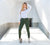 A woman modeling high-waisted green colombian leggings with built-in shapewear, standing in a sleek indoor setting.